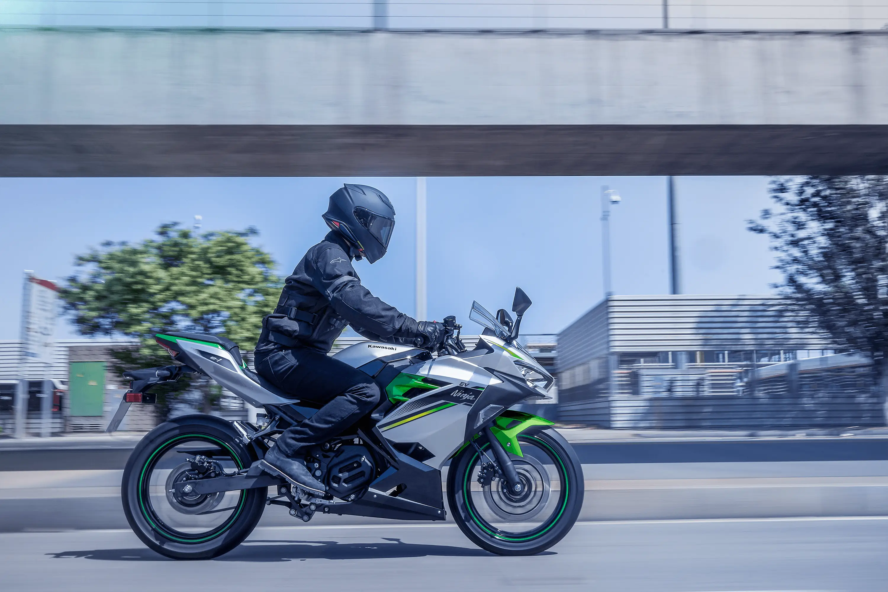 Side angle of a person riding a green motorcycle on a street.