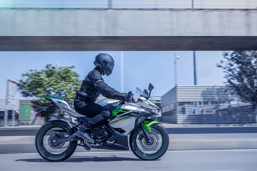 Side angle of a person riding a green motorcycle on a street. opens in a new window