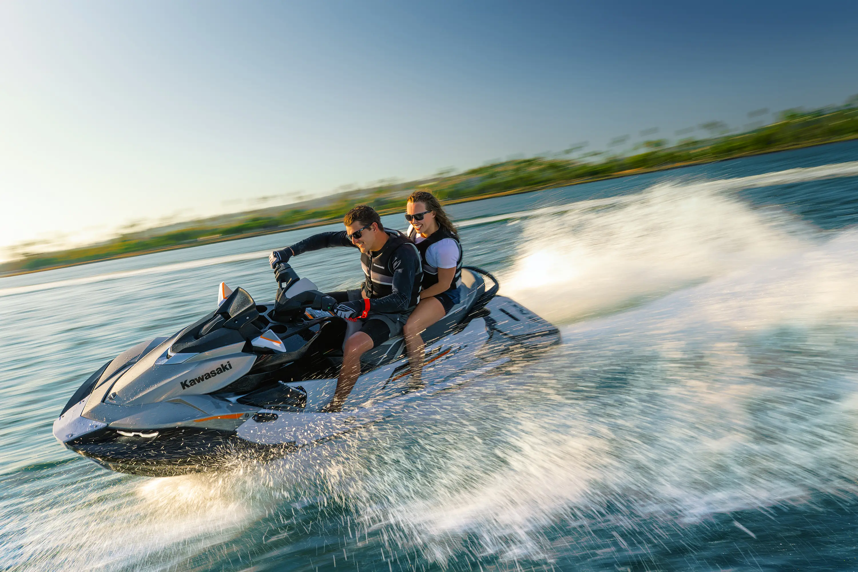 Side angle of two people turning on a personal watercraft on the water.