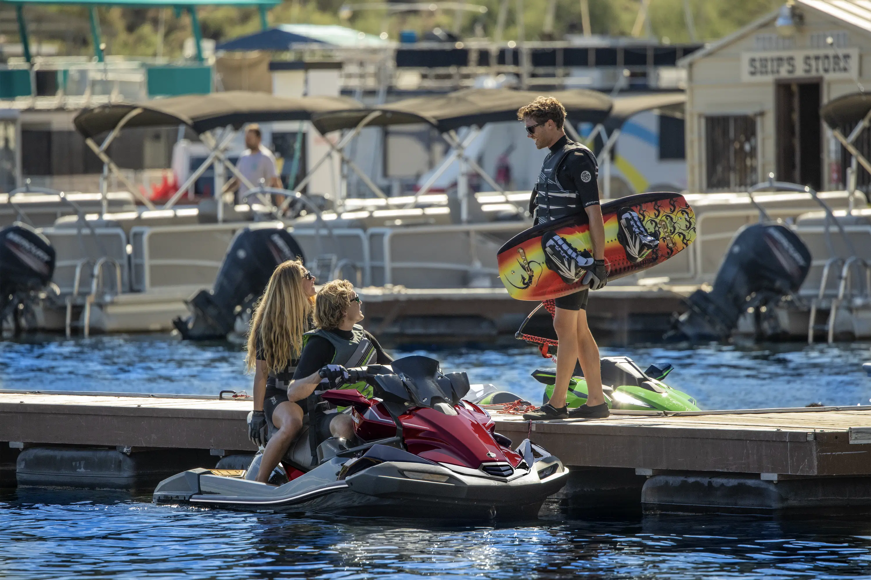 3 people at a dock with a personal watercraft on the water.