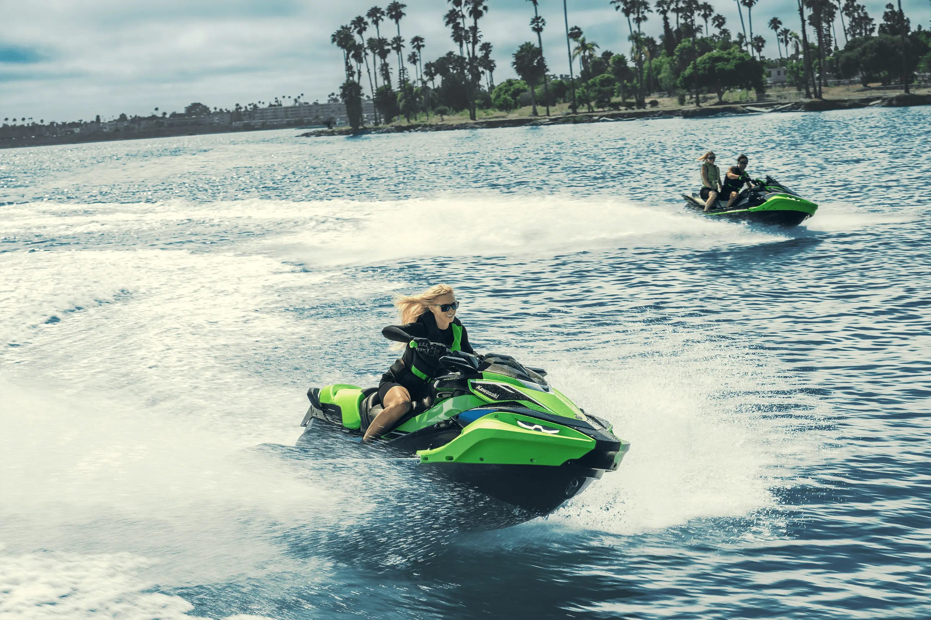 Three-quarter front angle of two people on two personal watercraft on the water.