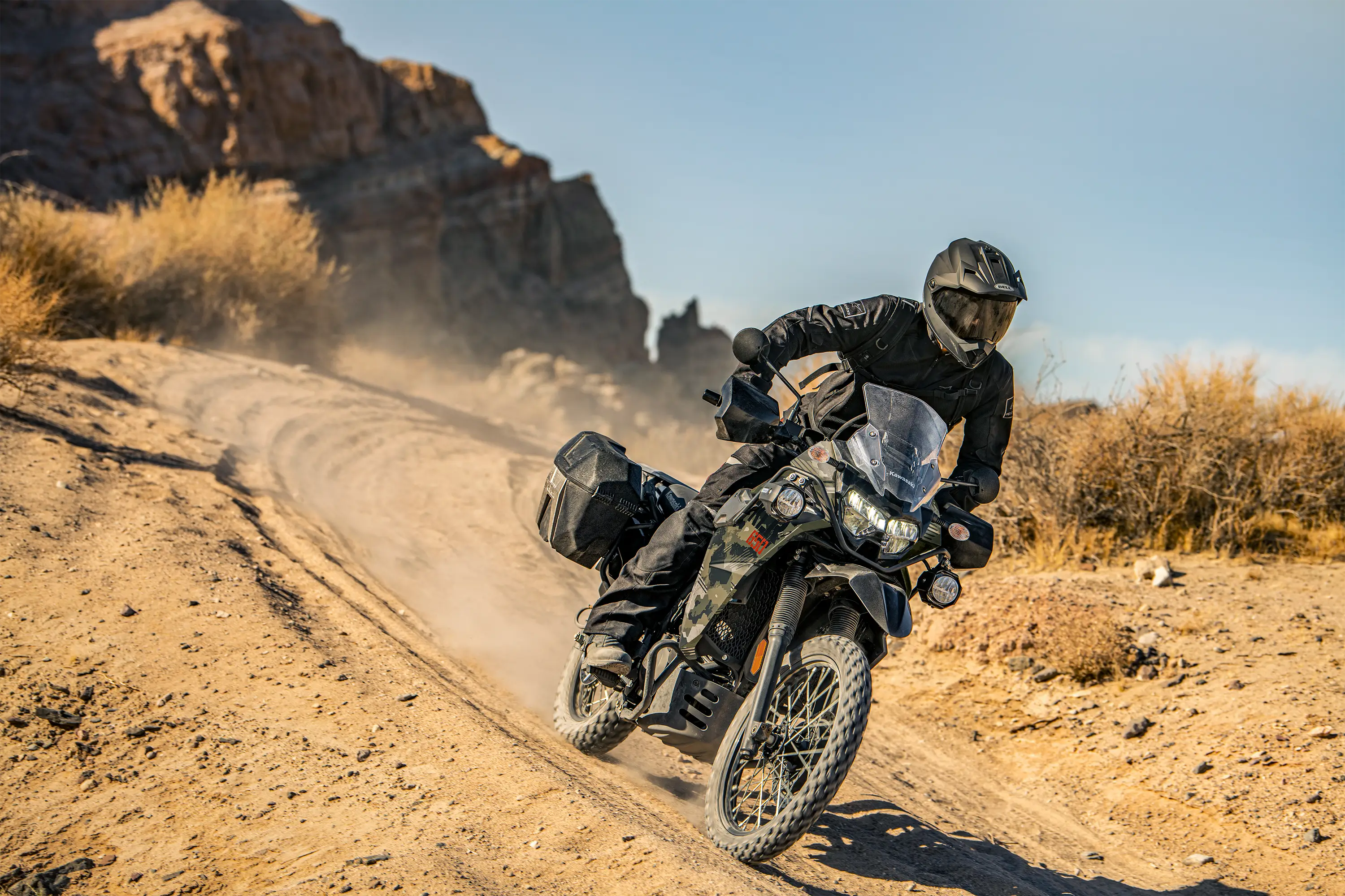 Three-quarter front angle of a person riding a motorcycle down a hill off-road.