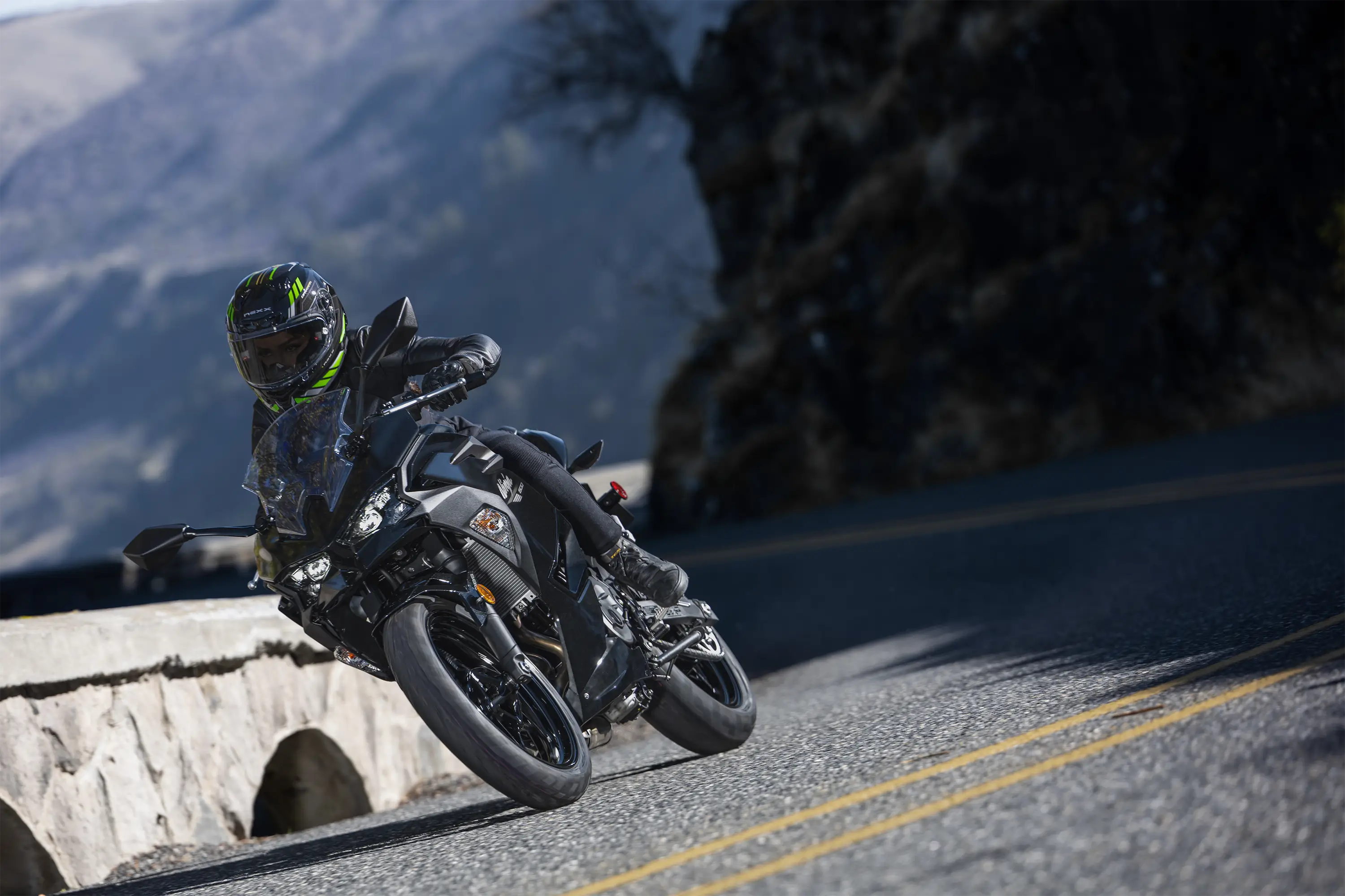 Three-quarter front angle of a person riding a motorcycle on a road.