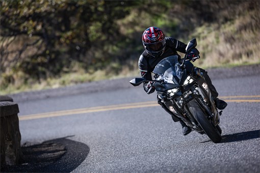 Front angle of a person riding a motorcycle around a bend in a road. opens in a new window