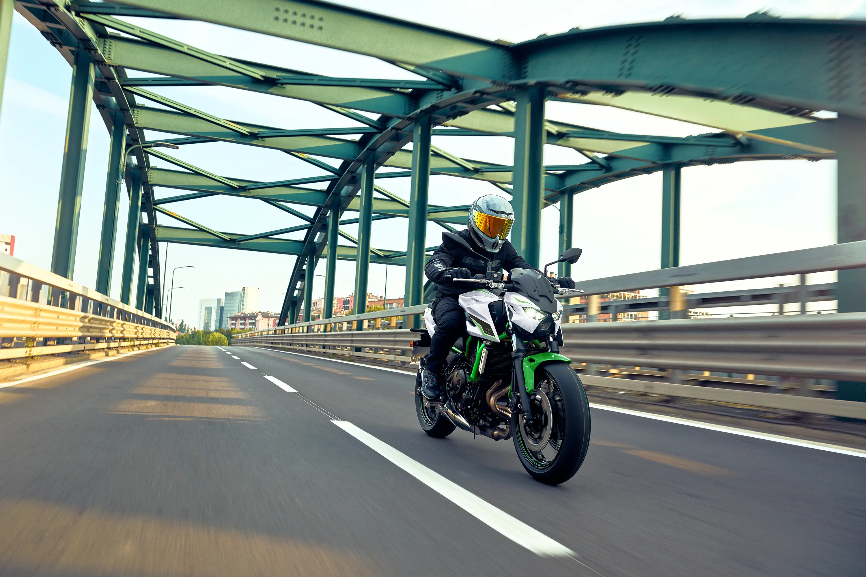 Three-quarter front angle of a person riding a motorcycle on a bridge.