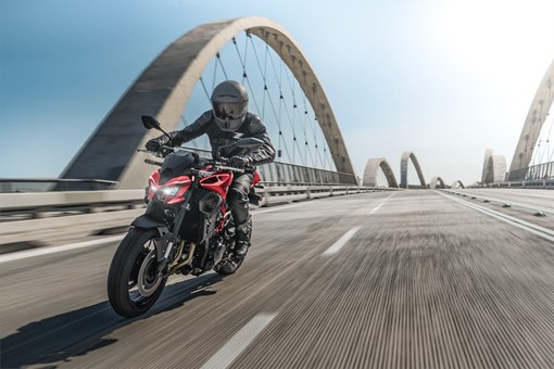 Three-quarter front angle of a person riding a motorcycle on a bridge. opens in a new window