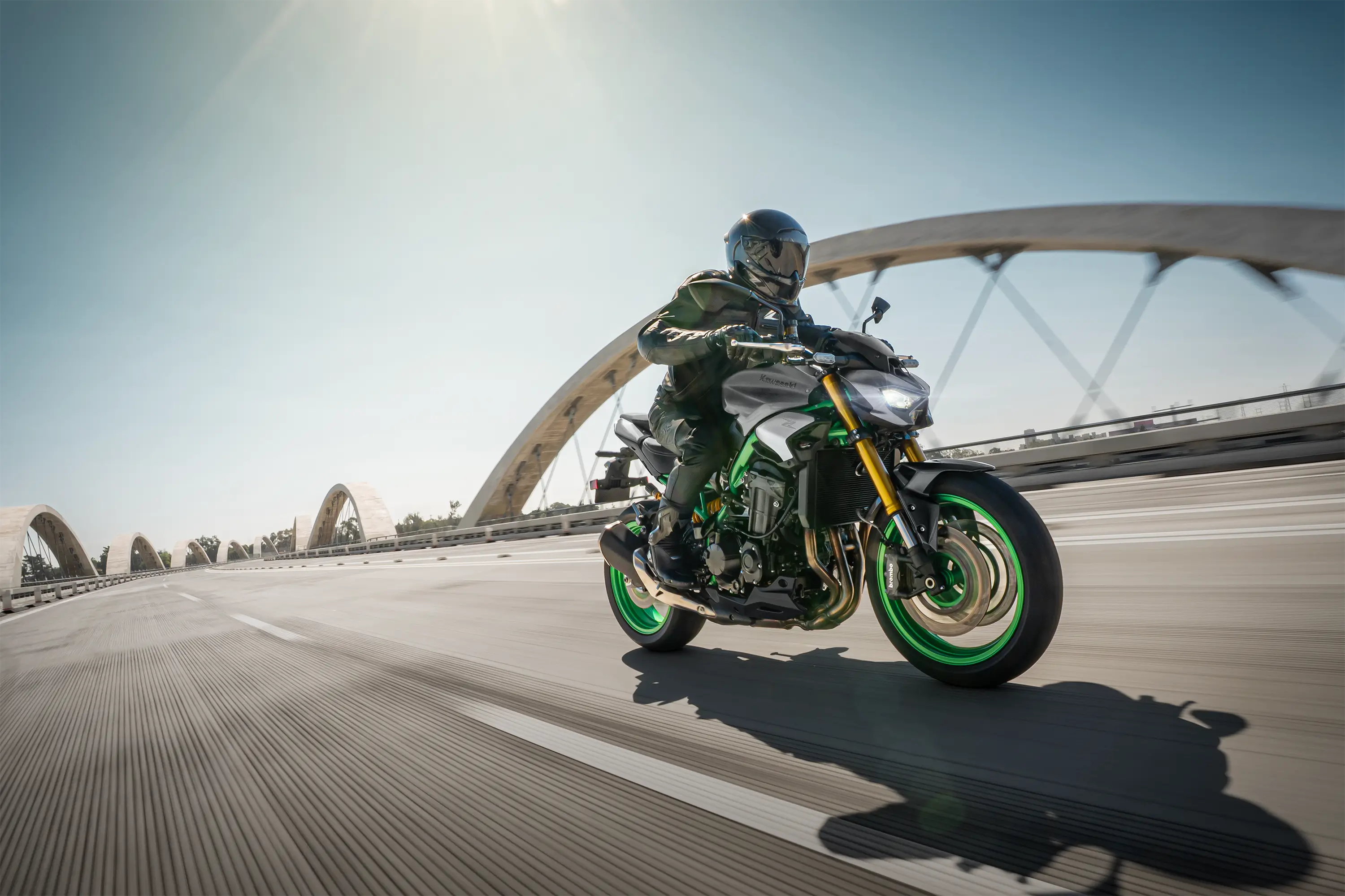 Three-quarter front angle of a person riding a motorcycle on a bridge.