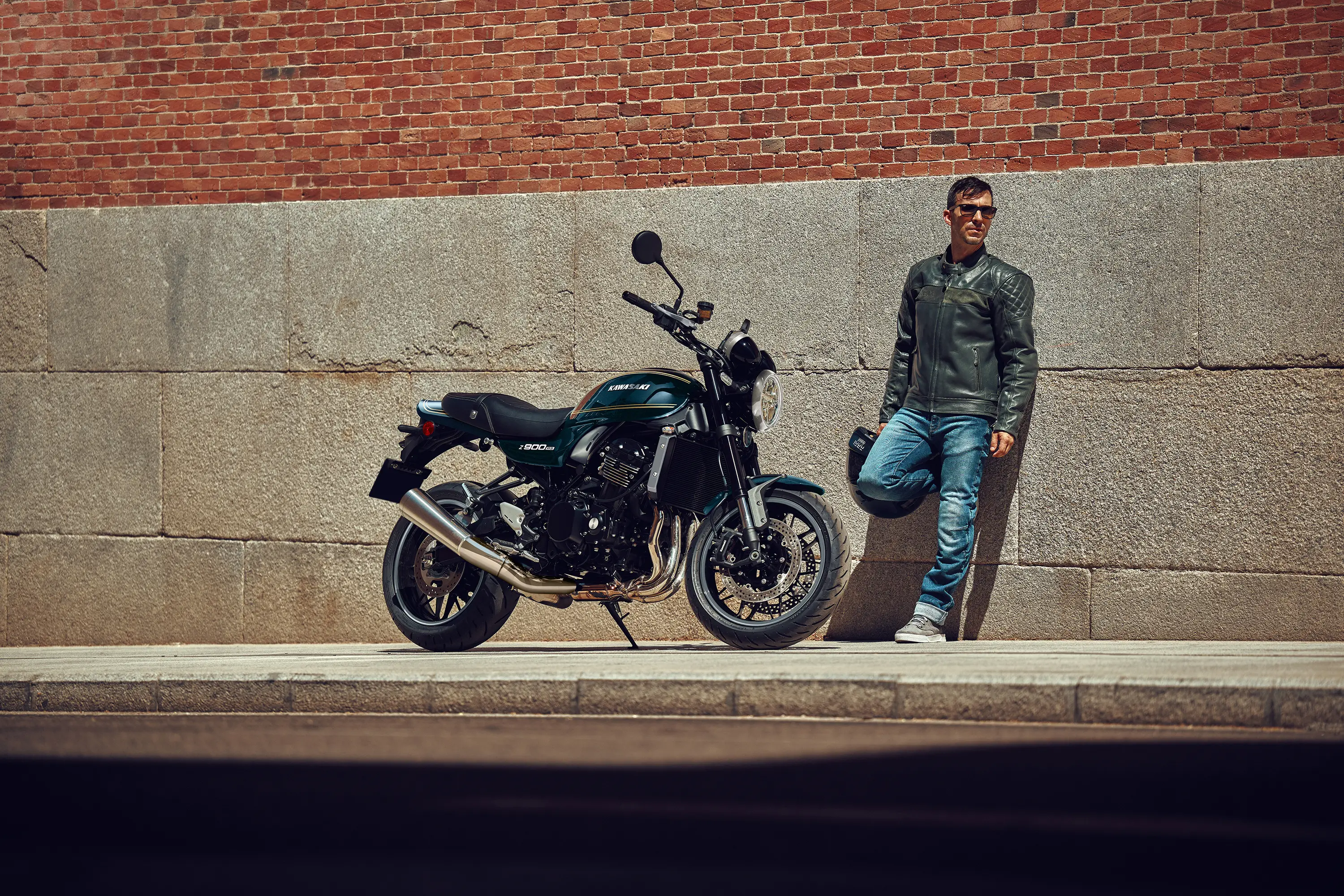 Side angle of a motorcycle parked on a city sidewalk near a person.