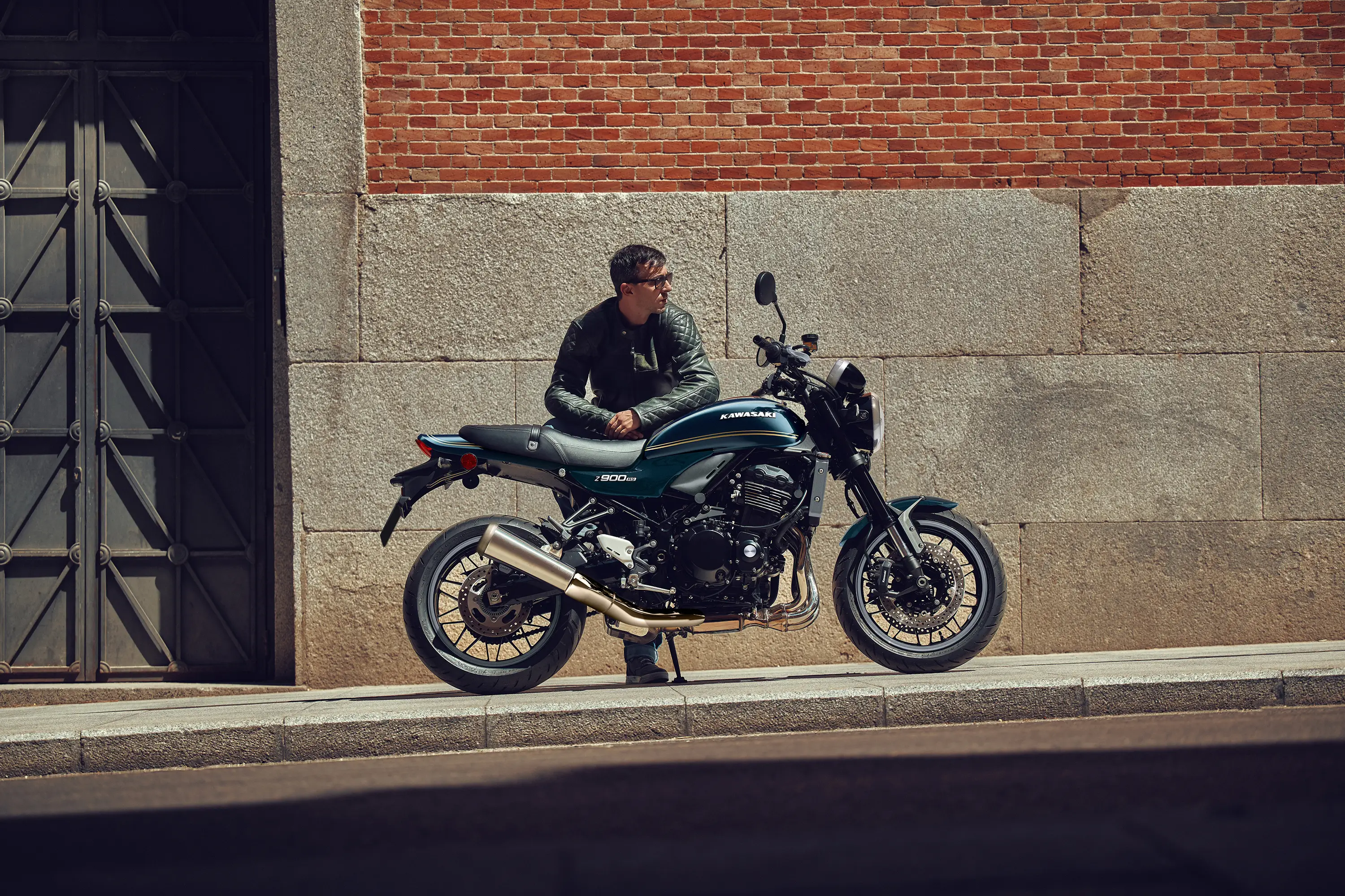 Profile angle of a motorcycle parked on a city sidewalk near a person.