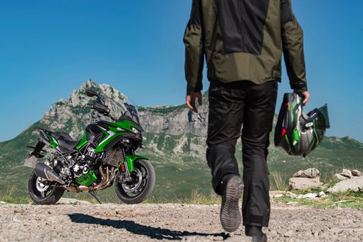 Three-quarter front angle of a motorcycle parked and rider walking toward. opens in a new window