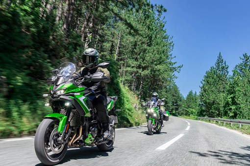 Three-quarter front angle of two people riding motorcycles on a highway. opens in a new window