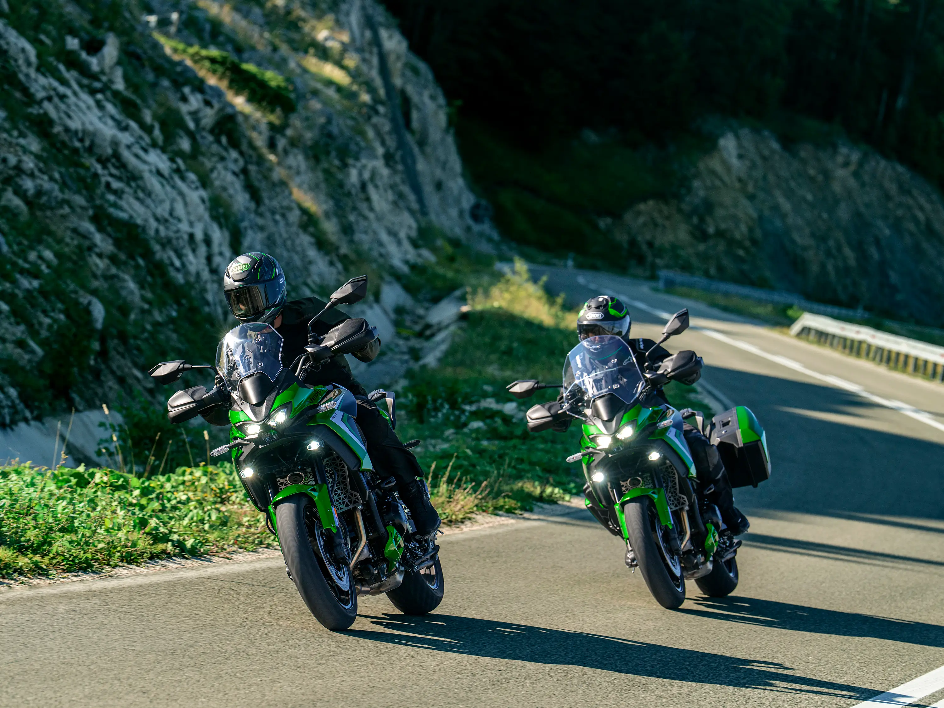 Front three-quarter angle of two people riding motorcycles around a turn.
