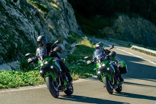 Front three-quarter angle of two people riding motorcycles around a turn. opens in a new window