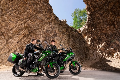 Three-quarter front angle of two motorcycles parked with riders. opens in a new window