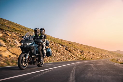 Three-quarter front angle of a person and a passenger riding a motorcycle on a highway. opens in a new window