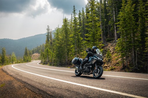 Three-quarter front angle of a person riding a motorcycle on a highway with trees in the background. opens in a new window