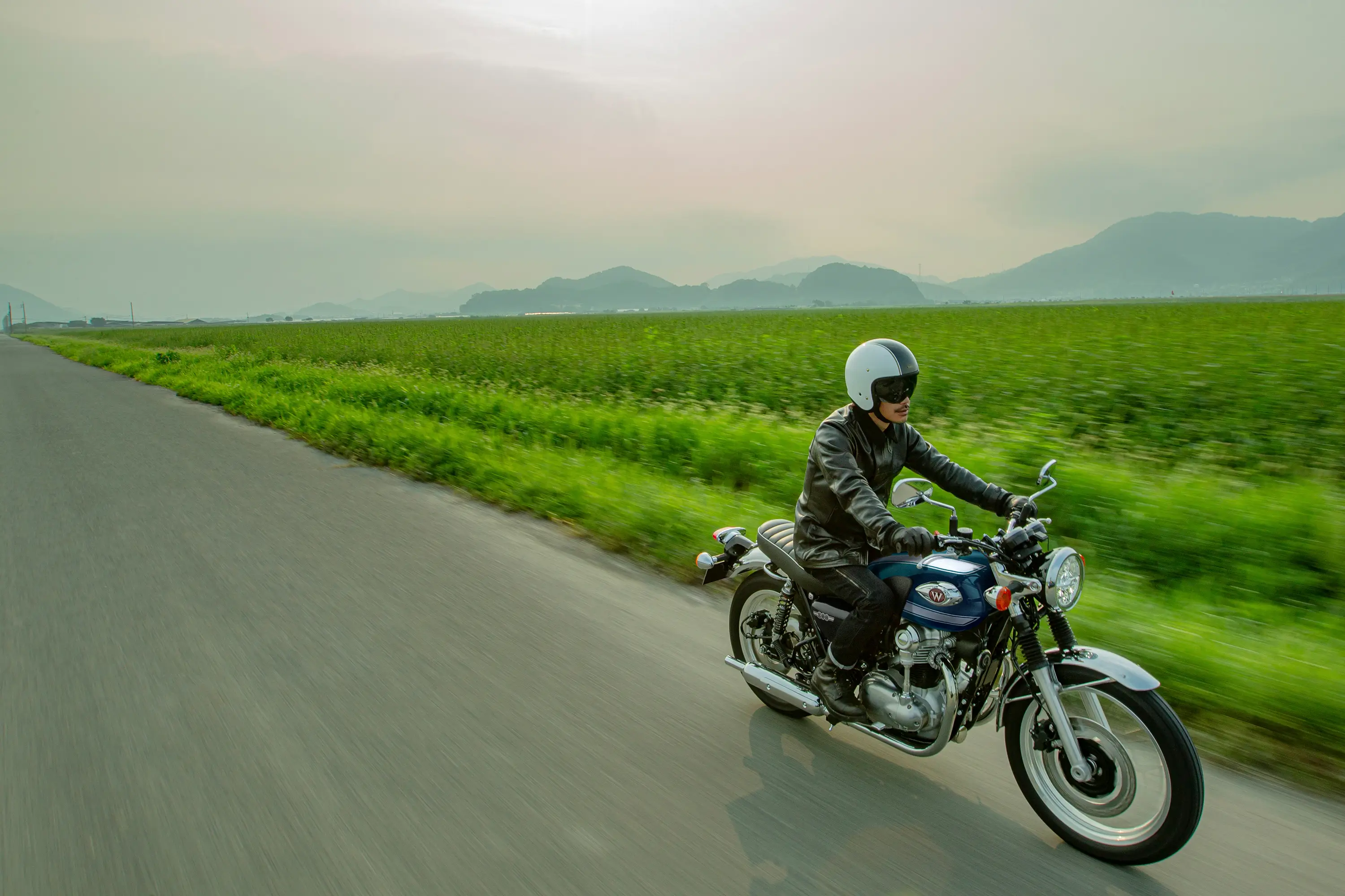 Three-quarter front angle of a person riding a motorcycle next to a field.
