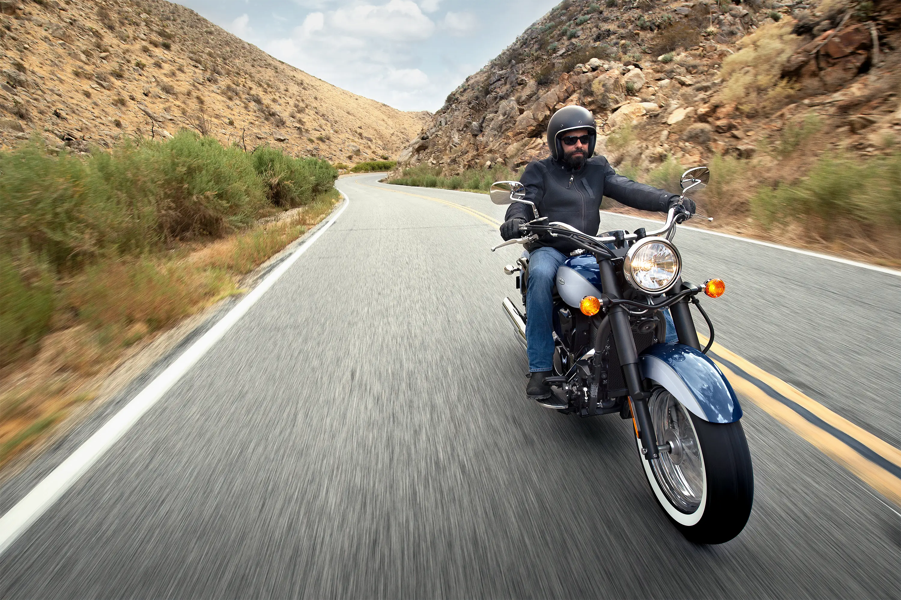 Front three-quarter angle of a person riding a motorcycle on a highway.