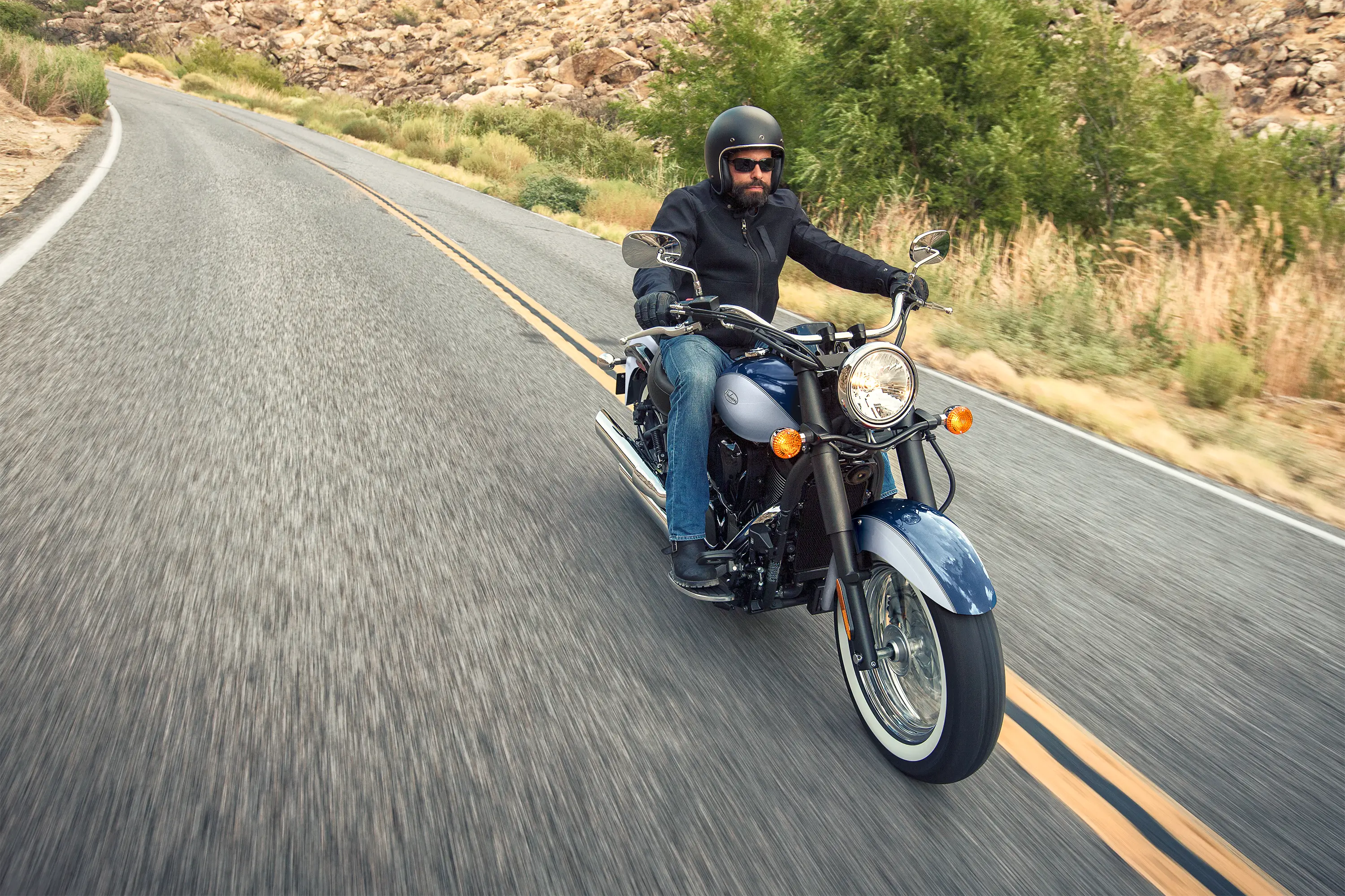 Front three-quarter angle from above of a person riding a motorcycle on a highway.