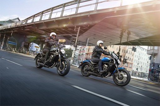 Three-quarter front angle of two people riding motorcycles on the street. opens in a new window