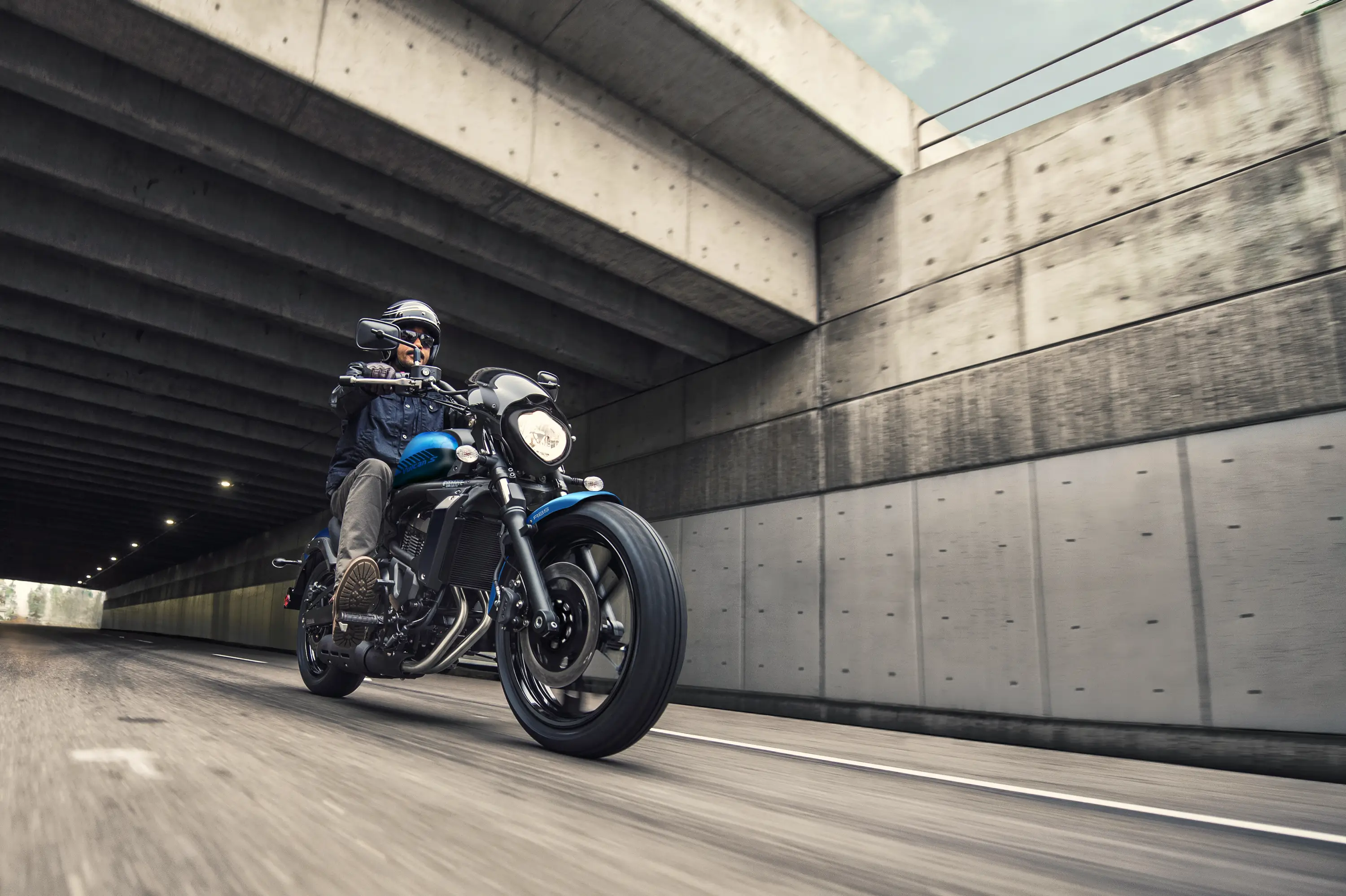 Three-quarter front angle of a person riding a motorcycle out of a tunnel.