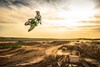 Three-quarter front angle of a person whipping a motorcycle high in the air on a track.