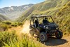 Three-quarter front angle of a person driving a side x side off-road up a hill.