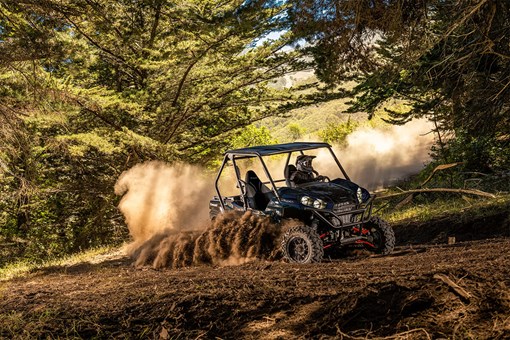 Three-quarter front angle of a person driving a side x side off-road through trees. opens in a new window