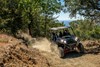 Three-quarter front angle of a person driving a side x side off-road through trees.