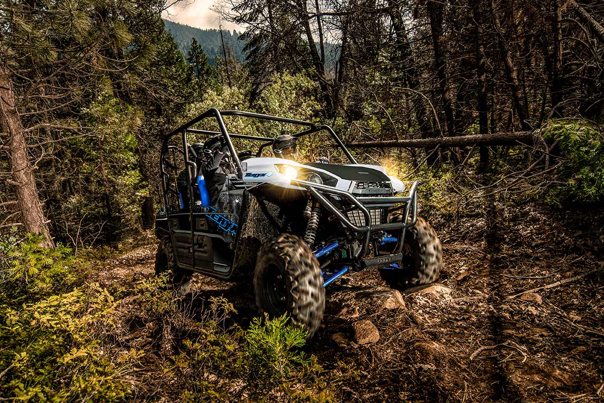 Side angle of a person and passengers driving a side x side off-road up hill.