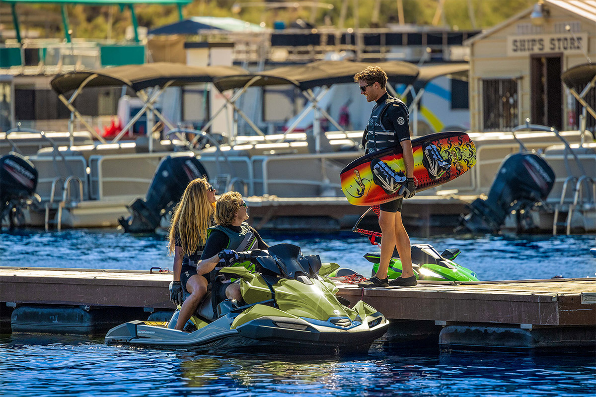 Three-quarter front angle of two people parked on a personal watercraft near a dock.