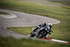 Three-quarter front angle of a person riding a motorcycle through a series of corners on a track.