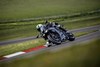 Three-quarter front angle of a person riding a motorcycle through a corner on a track with their leg out.