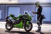 Side angle of a person standing in front of a motorcycle.