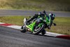 Three-quarter front angle of a person on a motorcycle leaning into a turn on a track.