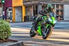 Three-quarter front angle of a person riding a motorcycle on a street.