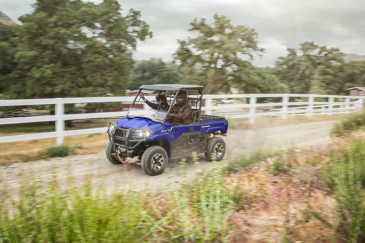 Three-quarter front angle of a person and passenger driving a side x side on a dirt trail.