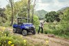 Three-quarter front angle of two people working next to a side x side parked on a trail.
