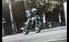 Three-quarter front angle of a person riding a motorcycle on a street.