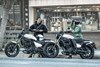 Side angle of two people next to and on motorcycles.