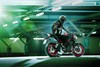 Three-quarter rear angle of a person seated on a motorcycle in a garage.
