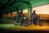 Three-quarter front angle of two people on motorcycles in a garage.