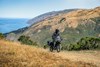 Three-quarter front angle of a person riding a motorcycle on a dirt trail.