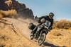 Three-quarter front angle of a person riding a green motorcycle on an off-road trail.