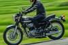 Side angle of a person riding a motorcycle on a road.
