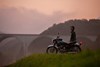 Profile angle of a person standing next to a parked motorcycle.