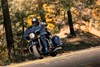 Three-quarter front angle of a person riding a blue motorcycle on a road.