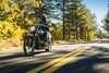 Three-quarter front angle of a person riding a gray motorcycle on a road.