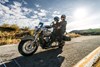 Side angle of a person and passenger riding a motorcycle on a road.