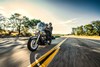 Three-quarter front angle of a person and passenger riding a gray motorcycle on a road.